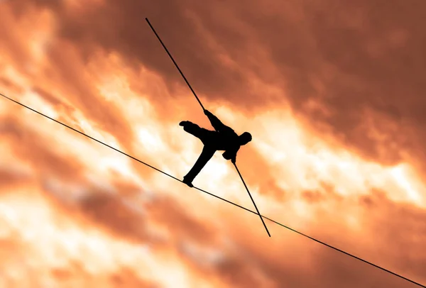 Wandering tightrope walker playing on  sky background. Silhouette of Equilibrist businessman with pole on the rope. idea concept of help and insurance, belay in business. Show in air