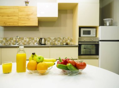Modern stil mutfak içinde sebzeler ve beyaz ahşap masada meyveler. Parlak beyaz mutfak ve ev eşyaları. Sağlıklı yaşam tarzı kavramı. Yiyecek ve içecek..