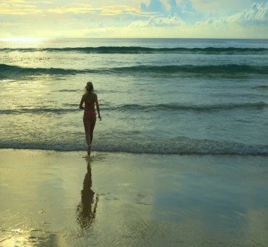 Arkadan bak. Okyanusa koşan kadın görüntüsü. Gün batımı. Deniz kıyısında koşan pembe mayo giymiş romantik bir kız. Güneşli sahil geçmişi. Dikiz aynası. büyük dalgalar.