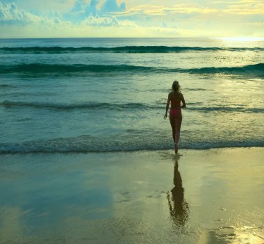Arkadan bak. Okyanusa koşan kadın görüntüsü. Gün batımı. Deniz kıyısında koşan pembe mayo giymiş romantik bir kız. Güneşli sahil geçmişi. Dikiz aynası. büyük dalgalar.