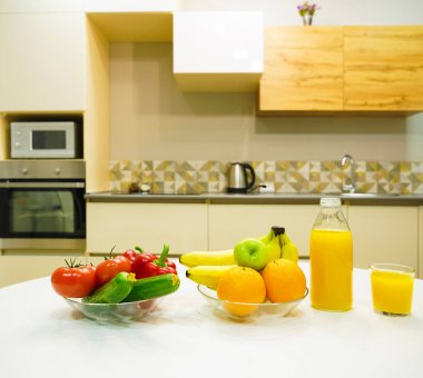 Modern stil mutfak içinde sebzeler ve beyaz ahşap masada meyveler. Parlak beyaz mutfak ve ev eşyaları. Sağlıklı yaşam tarzı kavramı. Yiyecek ve içecek..