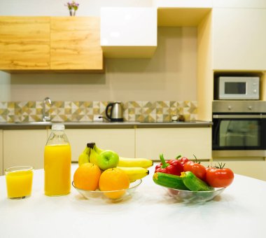 Modern stil mutfak içinde sebzeler ve beyaz ahşap masada meyveler. Parlak beyaz mutfak ve ev eşyaları. Sağlıklı yaşam tarzı kavramı. Yiyecek ve içecek..