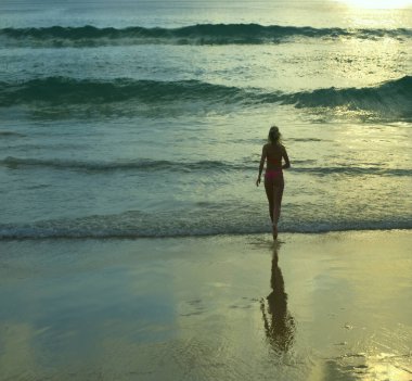 Arkadan bak. Okyanusa koşan kadın görüntüsü. Gün batımı. Deniz kıyısında koşan pembe mayo giymiş romantik bir kız. Güneşli sahil geçmişi. Dikiz aynası. büyük dalgalar.