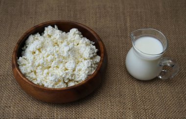 Yuvarlak ahşap tabakta süzme peynir. Çuval bezi kumaşında izole edilmiş. Yazı için boş kopyalama alanı. süt kavanozu