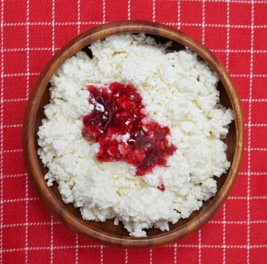 Yuvarlak ahşap tabakta süzme peynir. Arka planda kırmızı çizgili masa örtüsü. en üstteki görünüm