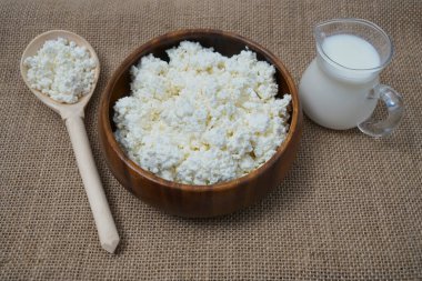 Yuvarlak ahşap tabak ve kaşıkla süzme peynir. Çuval bezi kumaşında izole edilmiş. Yazı için boş kopyalama alanı. dolu süt kavanozu
