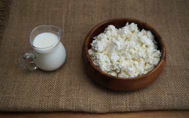 Yuvarlak ahşap tabakta süzme peynir. Çuval bezi kumaşında izole edilmiş. Yazı için boş kopyalama alanı. süt kavanozu