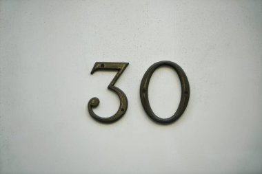 Beyaz taş duvarda 30 numaralı demir. Metal rakam 30 (30).