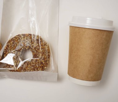 Paket paketinde bir çikolatalı çörek ve beyaz masada bir fincan kahve. Lezzetli çöller toz fındıkla kaplı, bir sokak fast food 'undan alınmış..