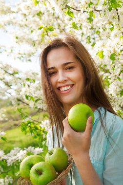 Baharda çiçek açan elma ağacının arka planında elinde elma tutan genç Latin kadının portresi. Yaz doğası. Bahar mevsimi. Çiçek açan bir elma dalının oluşumunda çok güzel.