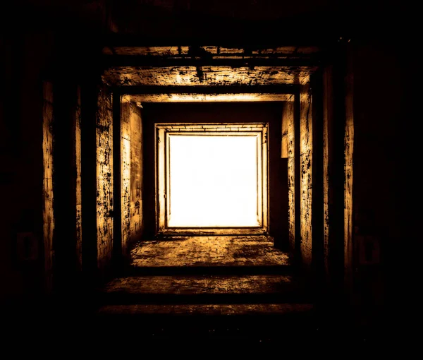 A square concrete drainage tunnel with a light at the end that shines from the turn of the tunnel. Empty square concrete tunnel. Dry abandoned military bunker. A light in the end of a tunnel