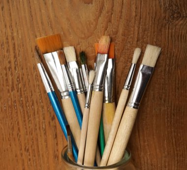 Ahşap masa arkasında izole edilmiş bir kavanozda bir sürü boya fırçası var..