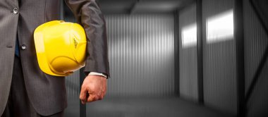 Sarı şapkalı mühendis. Metal yapının arka planına karşı işçi güvenliği için sarı miğfer tutuyor. Yüzü yok. Tamamlanmamış modern binalar. Metal tavan yapıları.