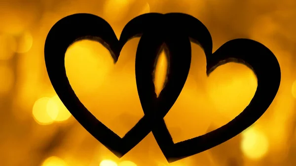 silhouette of black hearts  on yellow golden background. garland  lighting bokeh at night. backdrop wallpaper. blurred  backdrop. 2 two hearts . happy Valentines day. 14th february.