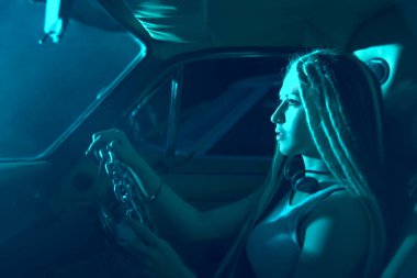 Kadın arabada direksiyon sallıyor ve uzaklara bakıyor. Yarış pilotu. Farlar yüzünde parlıyor. Gecenin ışığı. 