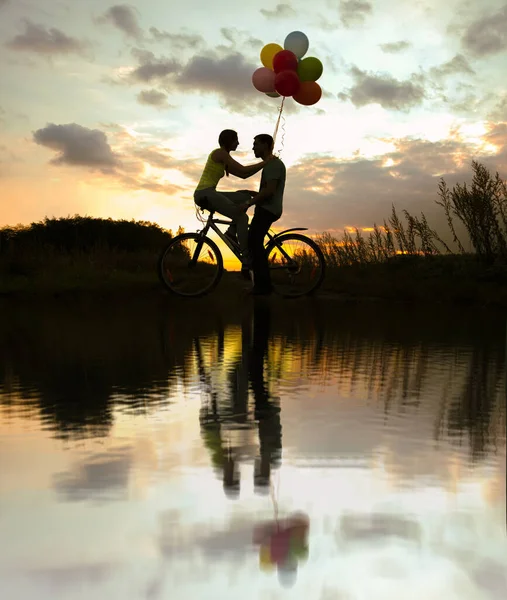 自転車に座っている2人の美しい大人のシルエット 日没時にカラフルな風船を持っている女の子 — ストック写真