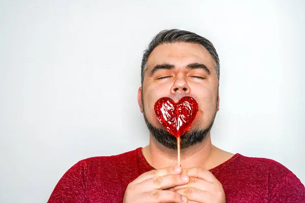 handsome man with red lollipops in the form of red heart. happy Valentines day idea. 14th february. funny male hides his lips  behind lollipop. closed eyes.