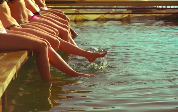 女性のグループは プールサイドで行に座っている 顔はない 少女たちのグループは 木製のプラットフォームでは 川の上に座っていると暖かい夏の日に水の中に足をはね 夏の季節 ビーチパーティー — ストック写真