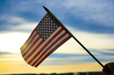 Yıldızlı ve çizgili Amerikan bayrağı mavi ve sarı günbatımı gökyüzüne karşı el ele tutuşuyor. 4 Temmuz. bağımsızlık günü.