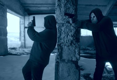 İki maskeli adam terk edilmiş binada silah taşıyor, kıyamet sonrası konsepti.