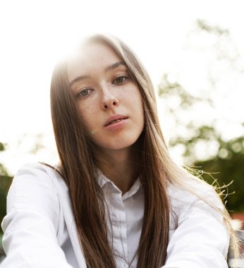 Beyaz tişörtlü çekici bir genç kadın gün batımında boş zamanlarının tadını çıkarıyor. Yazın genç bir kızın güzel portresi. Özgürlük yaşam tarzı ilkbahar konsepti. Arkaplanda güneş parıltısı