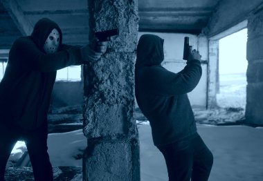 İki maskeli adam terk edilmiş binada silah taşıyor, kıyamet sonrası konsepti.