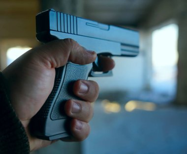 Erkek eli, arka planda siyah silah tutuyor. Yüzü yok.