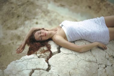 Çatlamış zeminde yatan güzel bir genç bayanın portresi. Kapalı gözler. Uzun kızıl saçlı kadın çatlak zeminde rüya görüyor.. 
