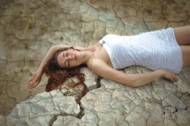 Çatlamış zeminde yatan güzel bir genç bayanın portresi. Kapalı gözler. Uzun kızıl saçlı kadın çatlak zeminde rüya görüyor.. 