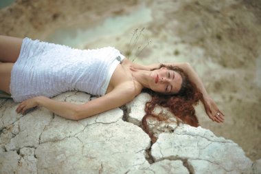 Çatlamış zeminde yatan güzel bir genç bayanın portresi. Kapalı gözler. Uzun kızıl saçlı kadın çatlak zeminde rüya görüyor.. 