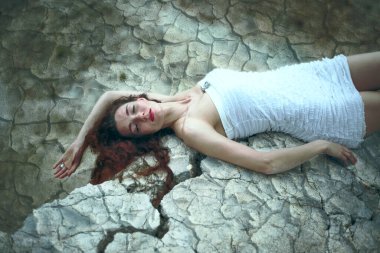Çatlamış zeminde yatan güzel bir genç bayanın portresi. Kapalı gözler. Uzun kızıl saçlı kadın çatlak zeminde rüya görüyor.. 