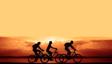Boşluk. Gün batımında bisiklete binen sportif arkadaşlar. Bisikletçiler sahil boyunca gidiyor. Doğa arka planında spor.