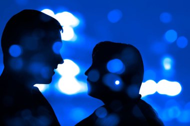 Gece şehir geçmişindeki genç çiftlerin siluetleri. Şehvetli çift öpüşüyor. renkli bokeh