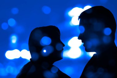 Gece şehir geçmişindeki genç çiftlerin siluetleri. Şehvetli çift öpüşüyor. renkli bokeh