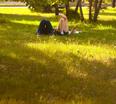  no faces. young couple in a park  on fresh green grass. spring time season. woman smoking cigarette near man. 
