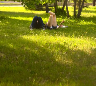  no faces. young couple in a park  on fresh green grass. spring time season. woman smoking cigarette near man. 