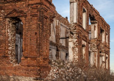 Penceresi kırık ve çatısı olmayan terk edilmiş bir bina. Tarladaki eski kırmızı tuğlalı ev. Gökyüzü zemininde birçok boş penceresi olan eski yıkılmış tuğla bina.