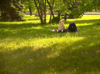  no faces. young couple in a park  on fresh green grass. spring time season. woman smoking cigarette near man. 