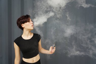 young girl smokes electronic cigarette. The model vaping a vaporizer in the studio.The face of vaping young woman at black studio. no smoking day