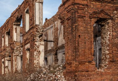 Penceresi kırık ve çatısı olmayan terk edilmiş bir bina. Tarladaki eski kırmızı tuğlalı ev. Gökyüzü zemininde birçok boş penceresi olan eski yıkılmış tuğla bina.