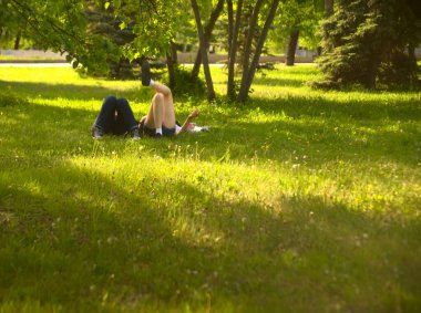  no faces. young couple in a park  on fresh green grass. spring time season. woman smoking cigarette near man. 