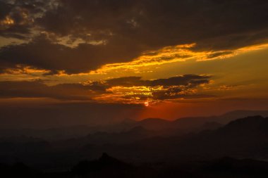 Dağlarda akşam manzarası var. Dramatik gün batımı. Güneş dağın arkasında batıyor ve güneş ışınları... 