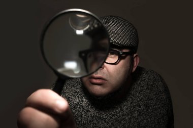 Okuma gözlüğü ve şapka takan bir adam büyüteçlere bakıyor. Siyah arkaplanda izole.