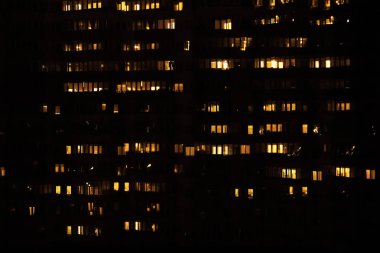 Çoklu aile konutları manzarası. Geceleri pencerelerinde ışık olan büyük bir apartman duvarındaki birçok pencere.