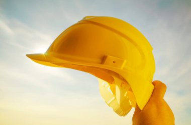 Güneşli arka planda sarı miğfer tutan mühendis. Güneş ışığı. güneş ışınları.