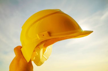 Güneşli arka planda sarı miğfer tutan mühendis. Güneş ışığı. güneş ışınları.