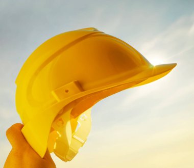 Güneşli arka planda sarı miğfer tutan mühendis. Güneş ışığı. güneş ışınları.