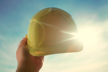 Güneşli arka planda sarı miğfer tutan mühendis. Güneş ışığı. güneş ışınları.