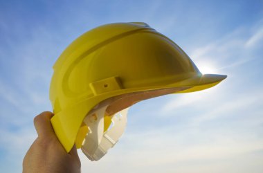 Güneşli arka planda sarı miğfer tutan mühendis. Güneş ışığı. güneş ışınları.