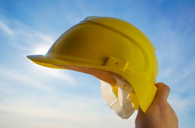 Güneşli arka planda sarı miğfer tutan mühendis. Güneş ışığı. güneş ışınları.